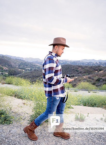 Junger Mann liest Smartphone-Text auf ländlichem Hügel