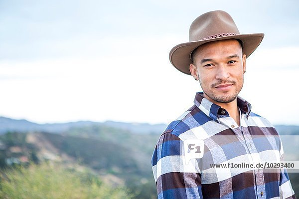 Porträt eines jungen Mannes mit Cowboyhut auf einem ländlichen Hügel