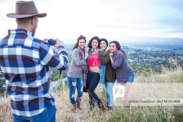 Young man photographing his four adult sisters on rural hill