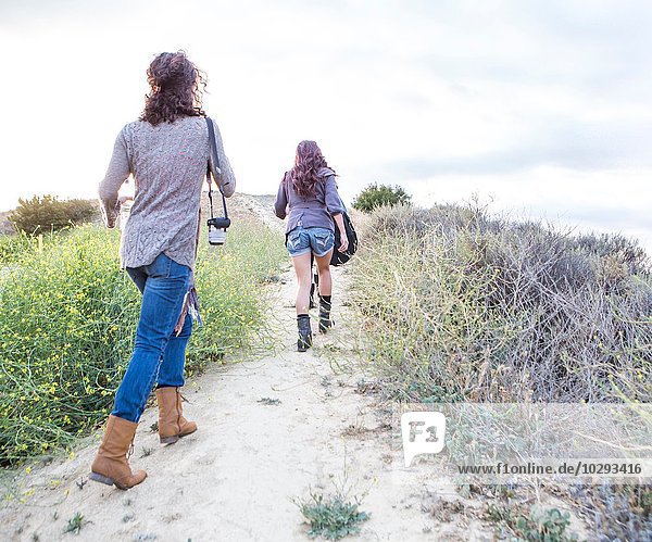 Rear view of two adult sisters walking along dirt track
