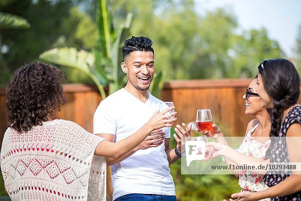 Young man sharing a rose wine toast with adult sisters in garden