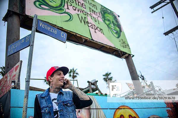Graffiti artist using smartphone under street signs  Venice Beach  California  USA