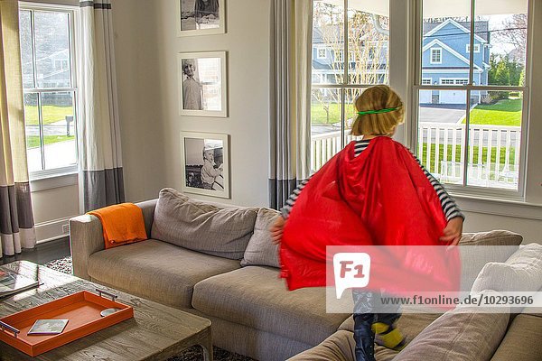 Boy with red cape playing on sofa