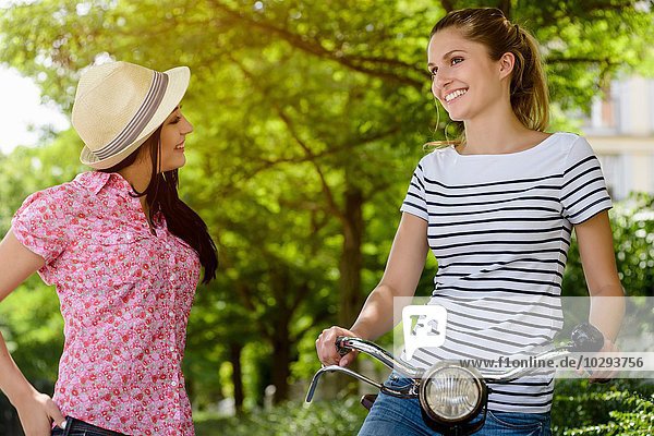 Junge Frau auf dem Fahrrad im Gespräch mit junger Frau mit Panamahut