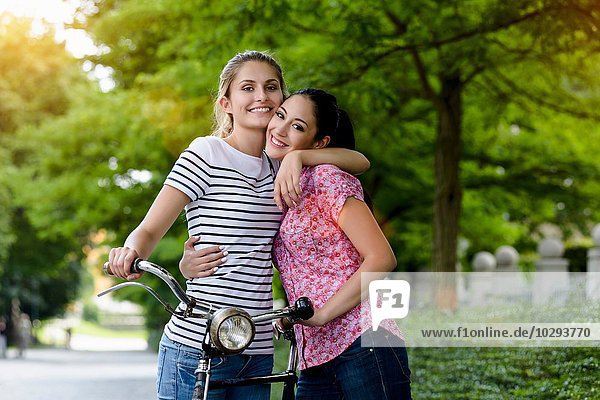 Porträt von jungen Frauen mit Fahrrad  Umarmung  Blick auf die Kamera lächelnd