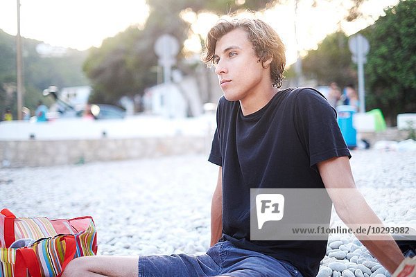 Junger Mann sitzt am Strand  Javea  Spanien