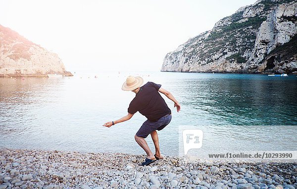 Rückansicht des jungen Mannes beim Abschöpfen von Steinen vom Strand  Javea  Spanien