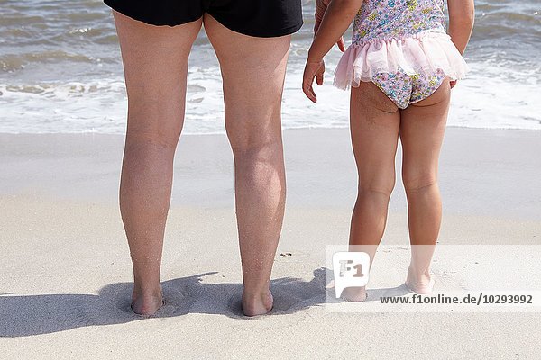 Blick von hinten auf die Beine der Seniorin und der Enkelin am Strand