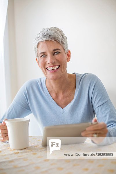 Porträt einer grauhaarigen  reifen Frau mit blauen Augen mit digitalem Tablett