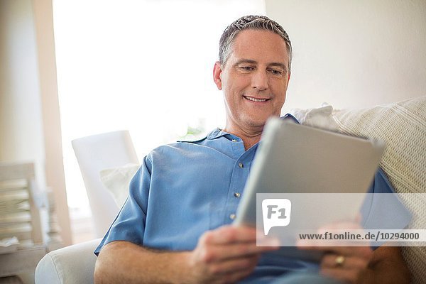 Erwachsener Mann liest digitales Tablett auf Sofa