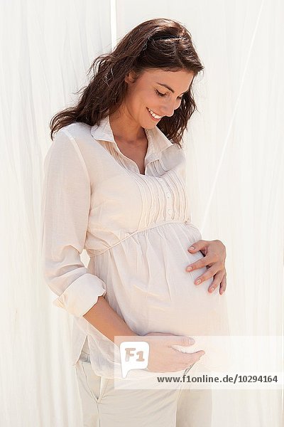 Eine schwangere erwachsene Frau  die auf ihren Bauch schaut.