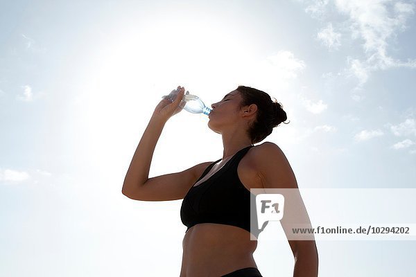 Niedriger Blickwinkel auf den blauen Himmel und die erwachsene Frau  die Wasser in Flaschen trinkt.