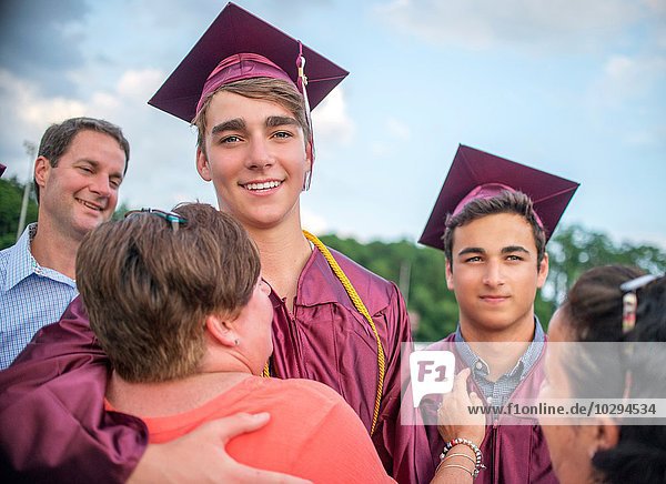 Zwei junge Männer umarmen Familie bei der Abschlussfeier