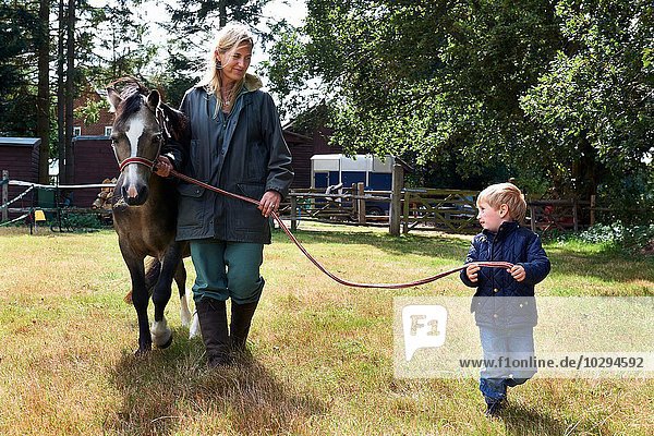 Kleiner Junge und Mutter führendes Pony im Feld