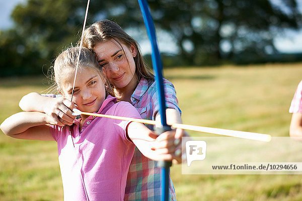 Mädchen lernen Bogenschießen von der Teenager-Schwester