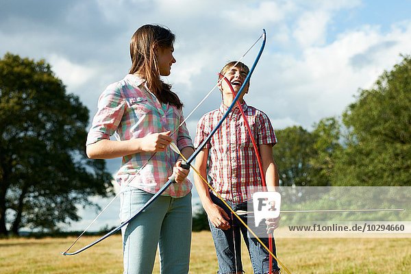 Teenage girl laughing with teenage brother whilst practicing archery