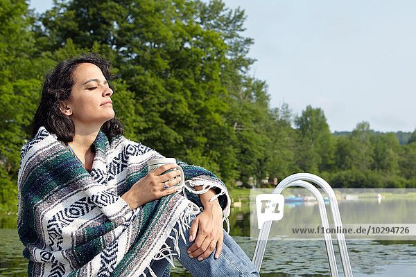 Woman wrapped in blanket sitting on lakeside  New Milford  Pennsylvania  USA