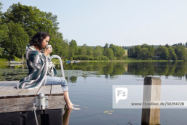 Woman wrapped in blanket sitting on lake pier  New Milford  Pennsylvania  USA