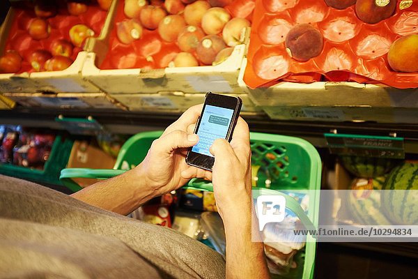 Mann einkaufen und Smartphone im Supermarkt benutzen