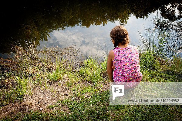 Rückansicht des Mädchens  das auf dem Flussufer hockt und Wasser sieht.