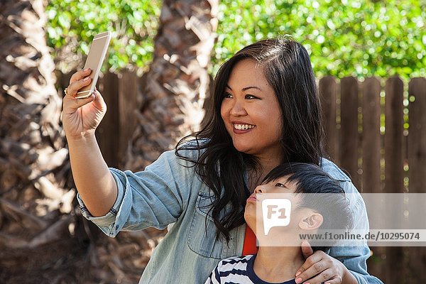 Mutter und Sohn posieren für Smartphone Selfie im Garten
