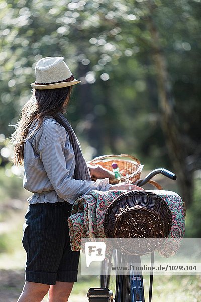 Reife Frau  die mit dem Fahrrad und Futterkörben in den Wald blickt