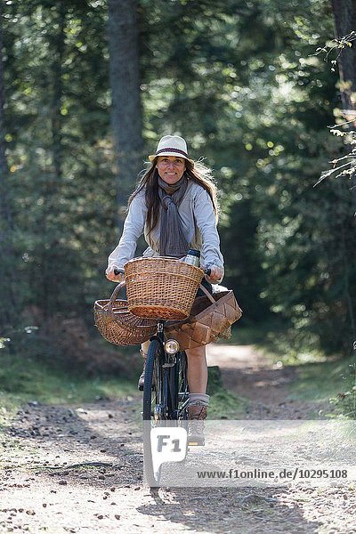 Mature woman cycling with foraging baskets on forest path