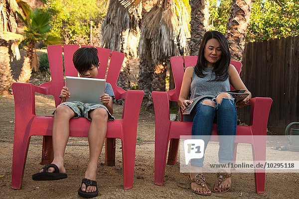 Junge und Mutter lesen digitales Tablett und Magazin im Garten