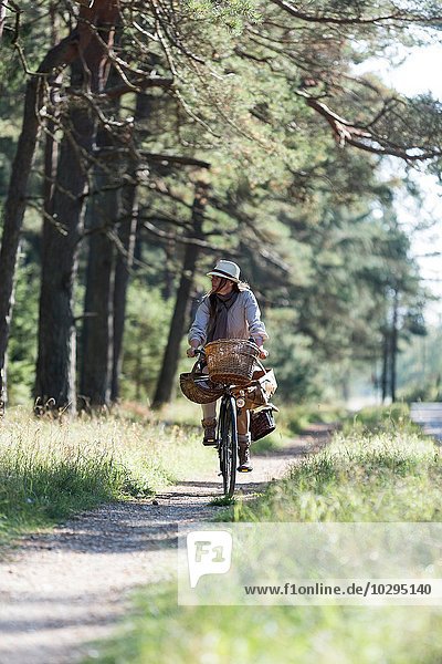 Woman cycling on forest path with foraging baskets