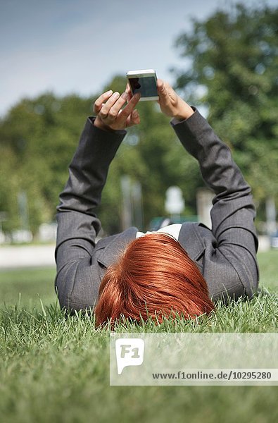 Oberflächenansicht einer mittelgroßen rothaarigen Frau auf Gras mit dem Smartphone