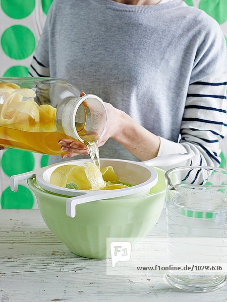 Mittelteil einer erwachsenen Frau  die Zitronen-Eistee aus einem Glas durch ein Sieb gießt.