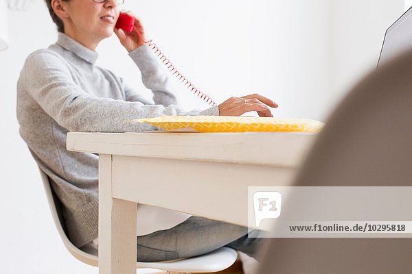 Schnittbild einer reifen Frau am Tisch mit Festnetztelefon  differenzierter Fokus