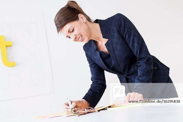 Reife Frau in Geschäftskleidung  die auf Papier schreibt und lächelnd nach unten schaut.