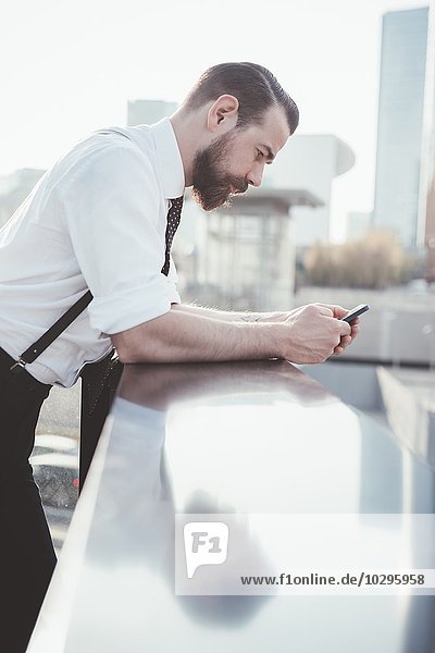 Stylish businessman reading smartphone text leaning against office balcony