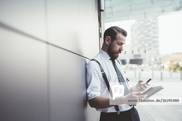 Stilvoller Geschäftsmann mit Smartphone und digitalem Tablett außerhalb des Büros