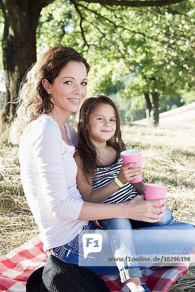 Portrait of mature woman and daughter drinking from paper cups at park picnic