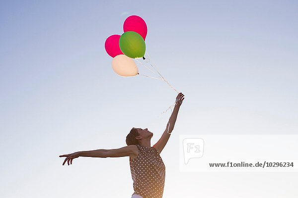 Flachwinkelansicht einer reifen Frau  die einen Haufen Luftballons gegen den blauen Himmel hält.