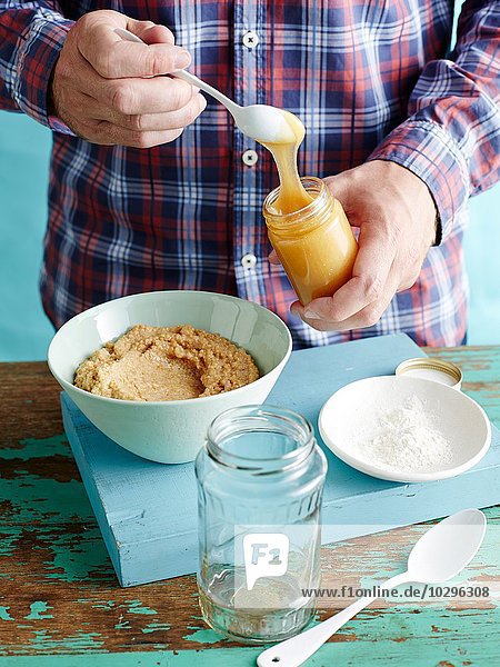 Mann bereitet frischen Senf Rezept Schritt 2  Hinzufügen von Honig zu gemischten Senfkörnern
