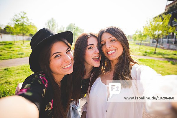Three young female friends posing for selfie in park
