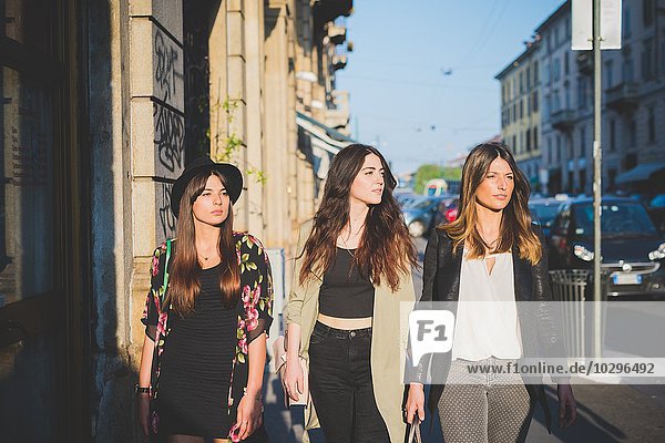 Drei junge Frauen  die auf der Straße spazieren gehen.