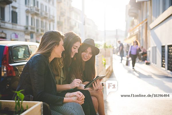 Drei junge Frauen sitzen mit digitalem Tablett auf der Stadtstraße