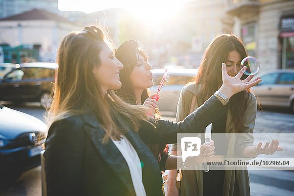 Drei junge Frauen blasen Blasen auf der Stadtstraße