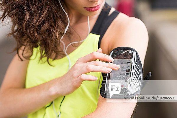 Beschnittene Nahaufnahme der Läuferin  die Musik auf dem Armband des Smartphones auswählt.