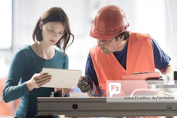 Male and female colleagues in industrial occupation using digital tablet