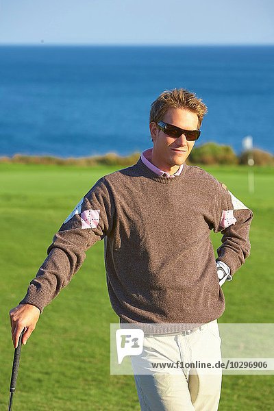 Golfer mit Sonnenbrille am Golfschläger  Hand an der Hüfte  Blick auf die Kamera