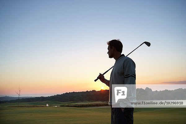 Golfer carrying golf club over shoulder looking at sunset