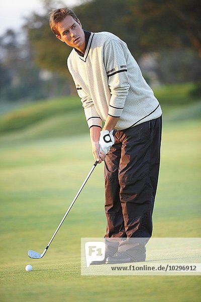 Golfer hält Golfschläger  der sich darauf vorbereitet  Goldschwung zu nehmen  und schaut weg.