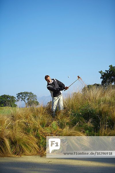 Golfer beim Golfschwung im hohen Gras  Golfball in der Luft