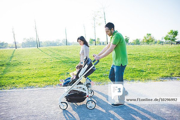 Mittleres erwachsenes Paar und Kleinkind-Tochter im Kinderwagen beim Spaziergang im Park