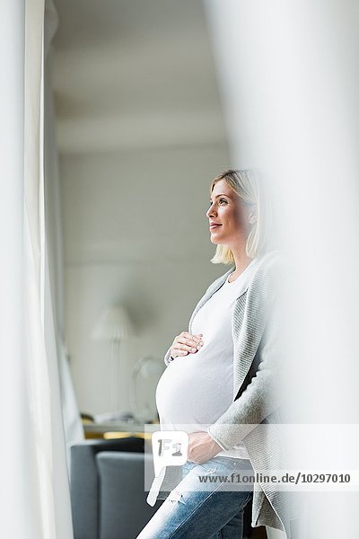 Vollzeitschwangerschaft junge Frau blickt aus dem Fenster